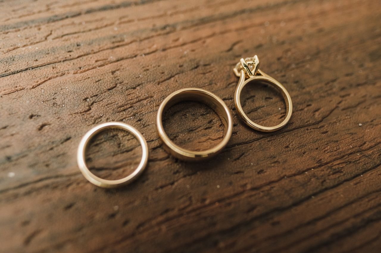 Three gold rings, including a diamond engagement ring, on a rustic wooden surface.