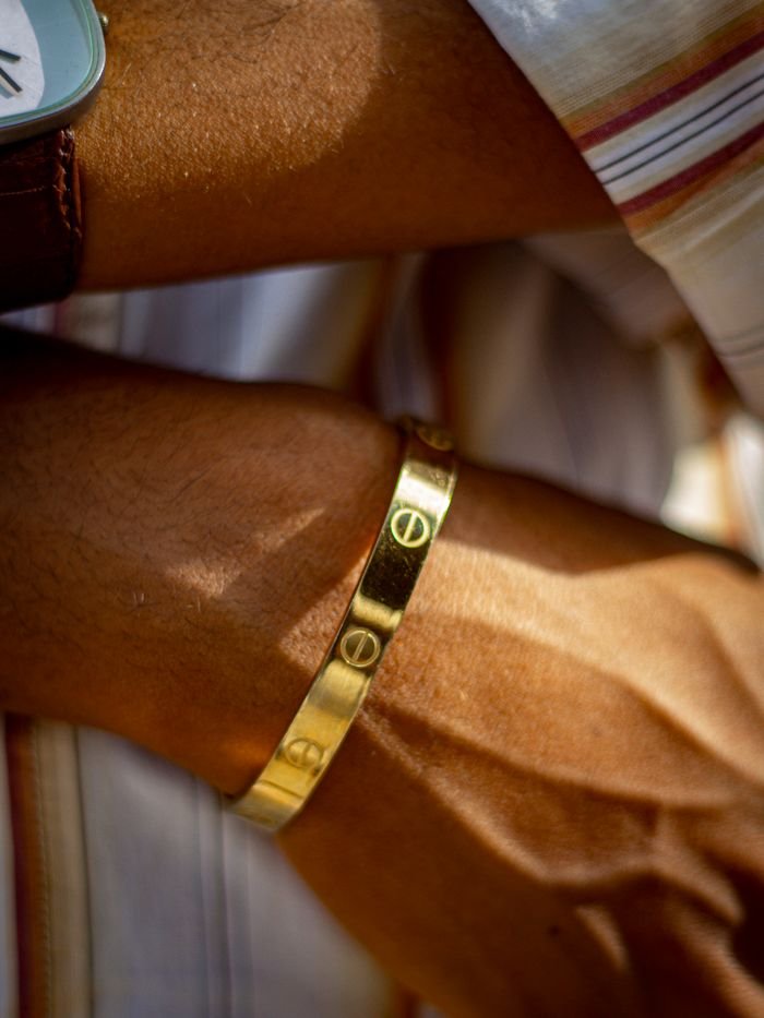 Arm with a gold bracelet and watch, wearing a striped shirt sleeve.